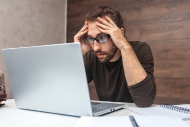 Sakallı, yorgun bir adam evde oturmuş laptopuyla uğraşıyor.