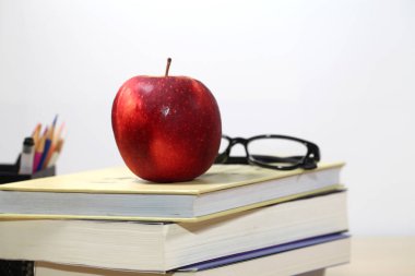 Masadaki okul malzemelerinin, Apple 'ın, masaüstündeki kitapların ve gözlüklerin birleşik resmi.