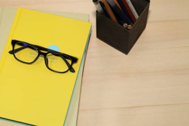 Masada okul malzemelerinin birleşik resmi, masaüstünde kitaplar ve gözlükler.