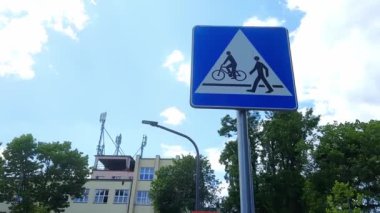 Pedestrian ve Bisiklet Geçidi işareti mavi gökyüzüne karşı. Beyaz üçgenli mavi kare üzerinde baston figürünün resmi ve bisikleti olan yol işareti.