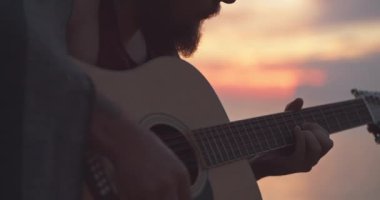 Sunriset'ta deniz kenarında gitar çalan adam