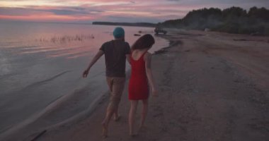 Erkek ve kadın el ele tutuşup sahilde yürüyor.