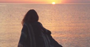 Gün batımında kıyıboyunca yürüyen kadın