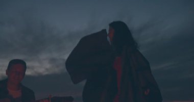 Gitar çalan bir adam ve şenlik ateşi yakınında dans eden kız