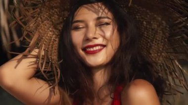 Sıcak yaz gününde hasır şapkalı ve kırmızı elbiseli güzel melez bir kadın. Güzel Asyalı kız gülümsüyor. Güzellik, seyahat, tatiller, moda konsepti ve yaşam tarzı.