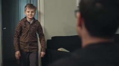 Genç baba sonunda işten eve geliyor. Babasına koşan ve ona sarılan sıradan giysili mutlu ergen oğlanın yakın çekimi. Gülümseyen oğul, akşam babasını kapıda karşılıyor. Mutluluk kavramı.