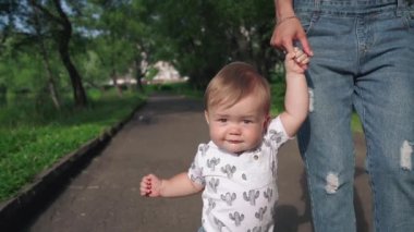 İlk adımları atan sevimli bir çocuğun portresi. Annelik kavramı. Güzellik annesi ve çocuğu parkta birlikte oynuyorlar. Güzel anne ve küçük oğlu dışarıda. Çocuk annesinin elini tutuyor..