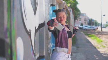 Yaratıcı kız sanatçı. Kültür özgürlüğü, tatil, yaşam tarzı konsepti. Genç ve güzel hippi kız sıcak yaz gününde şehrin banliyösünde grafiti duvarının önünde cep telefonuyla selfie çekiyor.