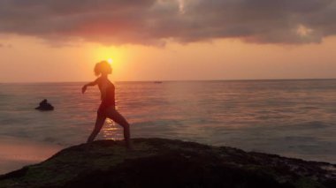 Sağlık kavramı, rahatlama, yoga. Mayo giymiş güzel bir kadın okyanus kıyısında yoga yapıyor. Dalgalar kuma vururken egzersiz yapan genç bir kızın silueti. Kadın gün ışığında meditasyon yapar..