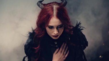 Büyücülük yapan korkunç bir iblis. Siyah boynuzlu kızıl saçlı cadı mum ışığında oturmuş ve elleri bağlı dua ediyor. Cadılar Bayramı gizemli ayini. Okültizm Ayini ya da Ezoterik Konsept.