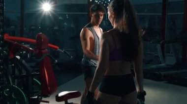 Dambılı atletik erkek ve kadın. Çekici kız ve erkek spor salonunda birbirlerine yardım ederler. Spor ve spor konusunda karşılıklı yardım. Güzel erkek ve seksi kadın spor malzemeleriyle antrenman yapıyorlar..