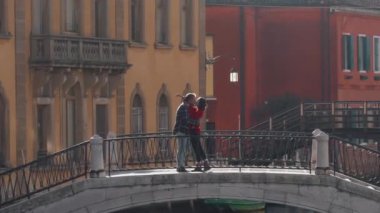 Yakışıklı bir adam, balayı sırasında Venedik köprüsünde duran Asyalı sevgilisini öpüyor ve sarılıyor. Tatili geçirmenin en iyi yolu Avrupa 'ya seyahat etmek..