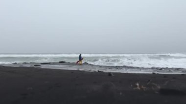 Kamçatka 'da inanılmaz bir snowboard deneyimi. Kar kaykaylı bir adam güzel kış gününde volkanik siyah kumsalda yürüyor. Tatil, doğa, tatil ve ekstrem spor kavramı.