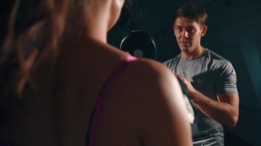 Genç esmer boksör ve antrenör. Atletik kız antrenörle tek başına çalışıyor. Erkek ve kadın kardiyo çalışması yapıyor. Adam kıza antrenman için yardım ediyor. Antrenman, güç, spor salonu kavramı.