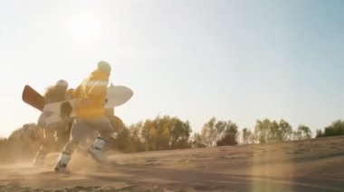 Üç neşeli çok ırklı arkadaş yaz tatilinin tadını çıkarıyor. Genç hippi adamlar ellerinde kumla gün batımında yüksekten koşuyorlar. Tatiller, spor, yolculuk, seyahat, mutluluk, arkadaşlık konsepti.