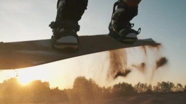 Genç ve güzel bir kadın kumsalda kumun üzerinde zıplıyor. Gün batımında snowboard 'a atlamaya çalışırken gülümseyen ve eğlenen bir kız. Spor konsepti, yaşam tarzı, kum kayağı, aşırı