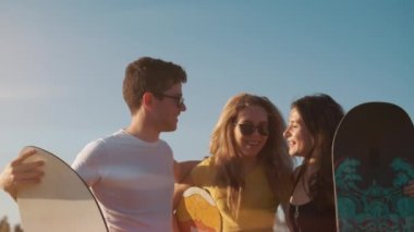 Açık havada yaz. Mutlu gülümseyen arkadaşlar, ellerinde snowboard ile güneşli bir akşamda beşlik atıyor. Çölde kum kaykayı. Gençler buluşuyor. Tatil, turizm ve ekstrem spor konsepti.