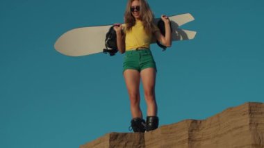 Güzel bir kız bir kum tepeciğinin kenarında elinde bir snowboard ya da kum kaykayıyla duruyor. Seksi bayan bir uçurumun kenarında tepiniyor. Kum yığını. Dağ gevşemesi. Özgürlük kavramı, yaşam tarzı.