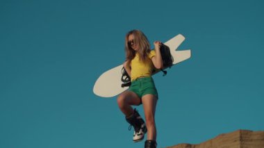 Seksi bayan bir uçurumun kenarında tepiniyor. Kum yığını. Güzel bir kız bir kum tepeciğinin kenarında elinde bir snowboard ya da kum kaykayıyla duruyor. Dağ gevşemesi. Özgürlük kavramı, yaşam tarzı.