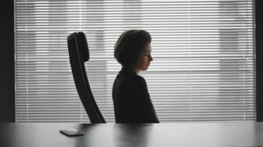 Ofisteki masadaki yorgun iş kadınının silueti. Kadın sandalyede hafifçe dönüyor ve başını tutuyor. Kız hayal kırıklığına uğramış ve çok çalışmış görünüyor. Meslek kavramı, stres, yorucu..