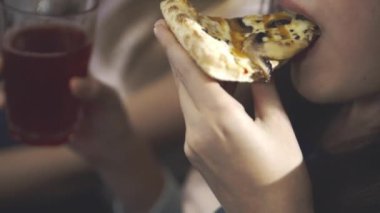 Arkadaşlar konuşur, güler, yemek dağıtırlar. Mutlu yüz ve elinde bir dilim pizza ve bardakla içki tutan bir kızın yakın çekimi. Oturma odasında pizza ve televizyonlu ev partisi..