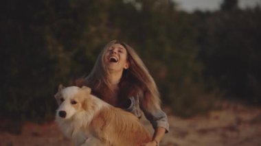 Border collie doggy kadın sahibinin üzerine atladı. Gün batımında deniz kenarında oynayan ve köpeğini kucaklayan bir sarışın. İzolasyon, arkadaşlık, tatil konsepti. Sonsuza dek arkadaşız.