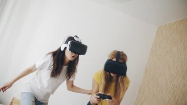 Üç boyutlu teknoloji. Sanal gerçeklik, oyun, arkadaşlık kavramı. Modern sanal gerçeklik kulaklıklarıyla video oyunları oynayan ve birlikte eğlenen iki kadın. Evde kasklı güzel kızlar var..