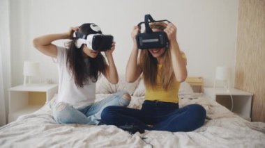 Evde kasklı, sanal gerçeklikte güzel kızlar var. İki kadın gördüklerine şaşırarak yatakta otururken sanal gerçeklik kulaklığı takıyor. Üç boyutlu teknoloji. Sanal gerçeklik, oyun, arkadaşlık kavramı.