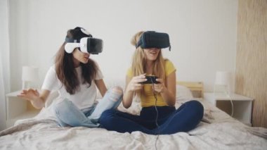 Evde sanal gerçeklik kasklı güzel kızlar var. Modern sanal gerçeklik kulaklıklarıyla video oyunları oynayan ve birlikte eğlenen iki kadın. Üç boyutlu teknoloji. Sanal gerçeklik, oyun, arkadaşlık kavramı.