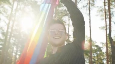 Homoseksüel bir adam güzel bir yaz gününde gökkuşağı bayrağı sallıyor. Kalp gözlüğü takan mutlu adam haklarını gösteriyor. LGBTQI, Gurur Etkinliği, LGBT Gurur Ayı, Eşcinsel Onur Sembolü