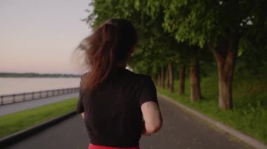 Kırmızı şortlu genç esmer nehir kıyısında koşuyor. Parkta koşan bir kadın. Yalnızlıktan ve sağlıklı yaşam tarzından hoşlanan bir kız. Solo aktivite kavramı, spor, maraton.