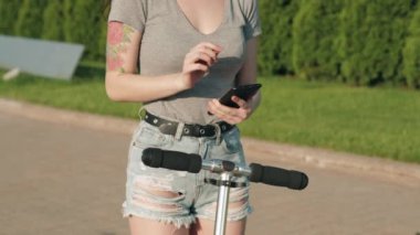 Güzel Asyalı kız akıllı telefondaki uygulamayla scooter 'ı kiralıyor. Kadın akıllı maaşla elektrikli scooter kiralıyor. Ekolojik toplu taşıma. Üniversite eko hayatı, aktif yaşam tarzı ve kiralama kavramı