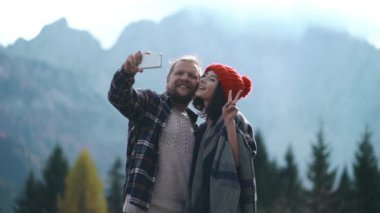 Yakışıklı adam ve güzel Asyalı kadın dağlıların önünde selfie çekiyorlar. Mutlu çift dışarıda birlikte vakit geçiriyor. Genç aile tatillerde doğada seyahat eder. Erkekler oto portre için telefon kullanır..
