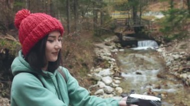 Dron ya da kuadrokopteri havaya fırlatan kızın yüzünün ve ellerinin yakın çekimi. Dağ nehrinin yakınında bir kadın İHA ya da helikopteri gökyüzüne gönderiyor. Kadın doğada yalnız zaman geçiriyor. Seyahat ya da turizm konsepti.