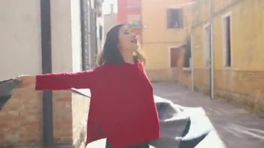 Küçük bir sokakta koşuşturan ve İtalya 'da maceralara hazır eğlenceli bir kız. Çekici genç Asyalı kadın şık kırmızı bir kazak giymiş çizgili pançosunu sallıyor ve öpücük yolluyor..