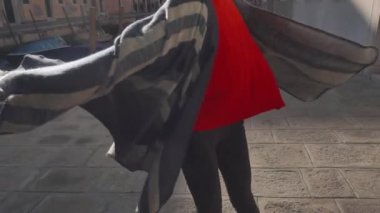 Kırmızı kazaklı ve çizgili pançolu mutlu Asyalı kadın Venedik sokaklarında neşeyle yürüyor. Çekici egzotik kız güneşin sıcaklığından zevk alıyor. Keyif ve rahatlama kavramı.