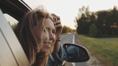 Kameraya gülümseyen şık bir kadın. Arabada oturan ve yolcu vagonunun camından sarkan güzel sarışın kızın portresi. Koyu renk saçları rüzgarda dalgalanıyor. Seyahat kavramı.