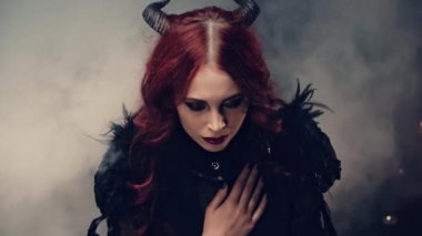 Büyücülük yapan korkunç bir iblis. Siyah boynuzlu kızıl saçlı cadı mum ışığında oturmuş ve elleri bağlı dua ediyor. Cadılar Bayramı gizemli ayini. Okültizm Ayini ya da Ezoterik Konsept.