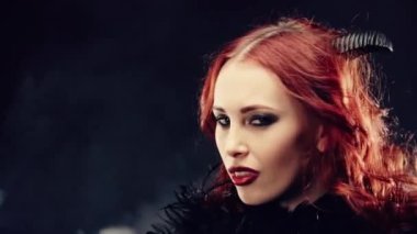 Kadın şeytani bir şekilde gülümsüyor ve büyü yapıyor. Kızıl saçlı ve şeytan boynuzlu bir cadı portresi. Karanlık güçler tarikatı, şeytan çağırma ayinleri, cadılar bayramı, okültizm, ezoterik.