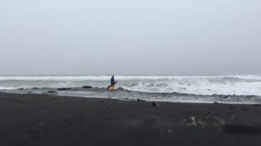 Kamçatka 'da inanılmaz bir snowboard deneyimi. Kar kaykaylı bir adam güzel kış gününde volkanik siyah kumsalda yürüyor. Tatil, doğa, tatil ve ekstrem spor kavramı.