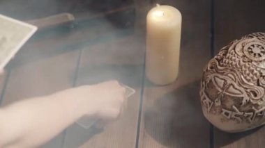 Falcının tarot kartlarını masaya koyduğu sahne. Kaderi ve geleceği kehanetle tahmin etmenin mistik ayini. Kaderi tahmin eden kadın dumanlı mum dolu karanlık odayı aydınlatıyor. Esrarengiz kavram.