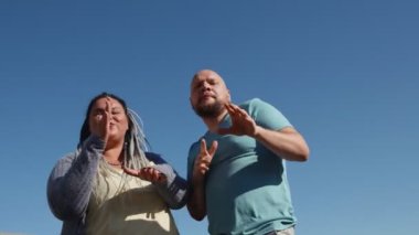 Vücut pozitif şişman arkadaşlar hayatın ve güneşli havanın tadını çıkarırlar. İki genç mutlu insan, parlak mavi gökyüzünün arka planında dans ediyor. Müzik ve kopyalama uzay konsepti. Dövmeli bir adam ve dans eden bir kadın..