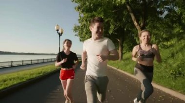 Nehir kenarında eğitim gören üç çok ırklı genç insan. Arkadaşlar birlikte vakit geçiriyorlar. Kızlar ve erkek sabah parkta süratle koşuyorlar. Açık havada antrenman yapan adamlar. Sağlık kavramı.
