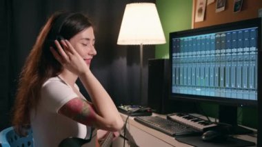 Yaratıcılık sürecinin tadını çıkaran bir kız. Ev kayıt stüdyosunda hafif sinematik ışıkta bayan müzisyen şarkısı. Gitar çalan ve sentezleyen genç bir kadın eşitleyici programı kullanarak müzik yaratıyor..