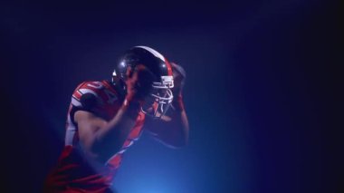 Parlak stadyum ışıkları altında kasklı kararlı profesyonel Amerikan futbolcusunun portresi topu yakalıyor. Üniformalı kendinden emin bir adam. Usa takım oyunu ve ekstrem spor ruhu konsepti.