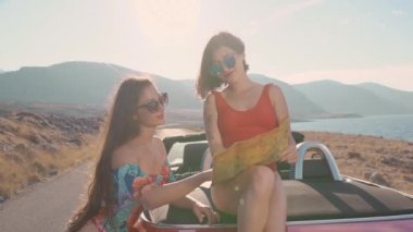 Cabriolet 'te haritayı araştıran gözlüklü iki çekici kız. Seyahat, yaşam tarzı. Lüks, özgürlük, blog konsepti. Sony, 4k, 10 bit renk