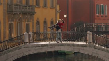 Yakışıklı bir adam, balayı sırasında Venedik köprüsünde duran Asyalı sevgilisini öpüyor ve sarılıyor. Tatili geçirmenin en iyi yolu Avrupa 'ya seyahat etmek..