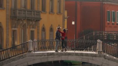 Yakışıklı bir adam, balayı sırasında Venedik köprüsünde duran Asyalı sevgilisini öpüyor ve sarılıyor. Tatili geçirmenin en iyi yolu Avrupa 'ya seyahat etmek..