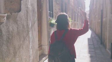 Maceracı Asyalı kadının Venedik, İtalya 'da akıllı telefonuyla küçük rahat caddelerin videosunu kaydettiği arka manzara. Kadın sırt çantası Instagram 'ı için ilginç materyaller hazırlıyor. Blogger hayatı