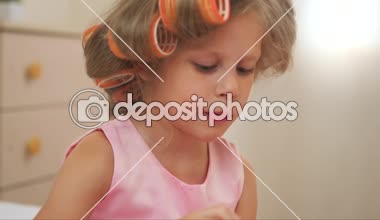 Güzel kız manikür yaparken curlers içinde. Yatağın üstüne oturan küçük prenses pembe elbise boyama nails.